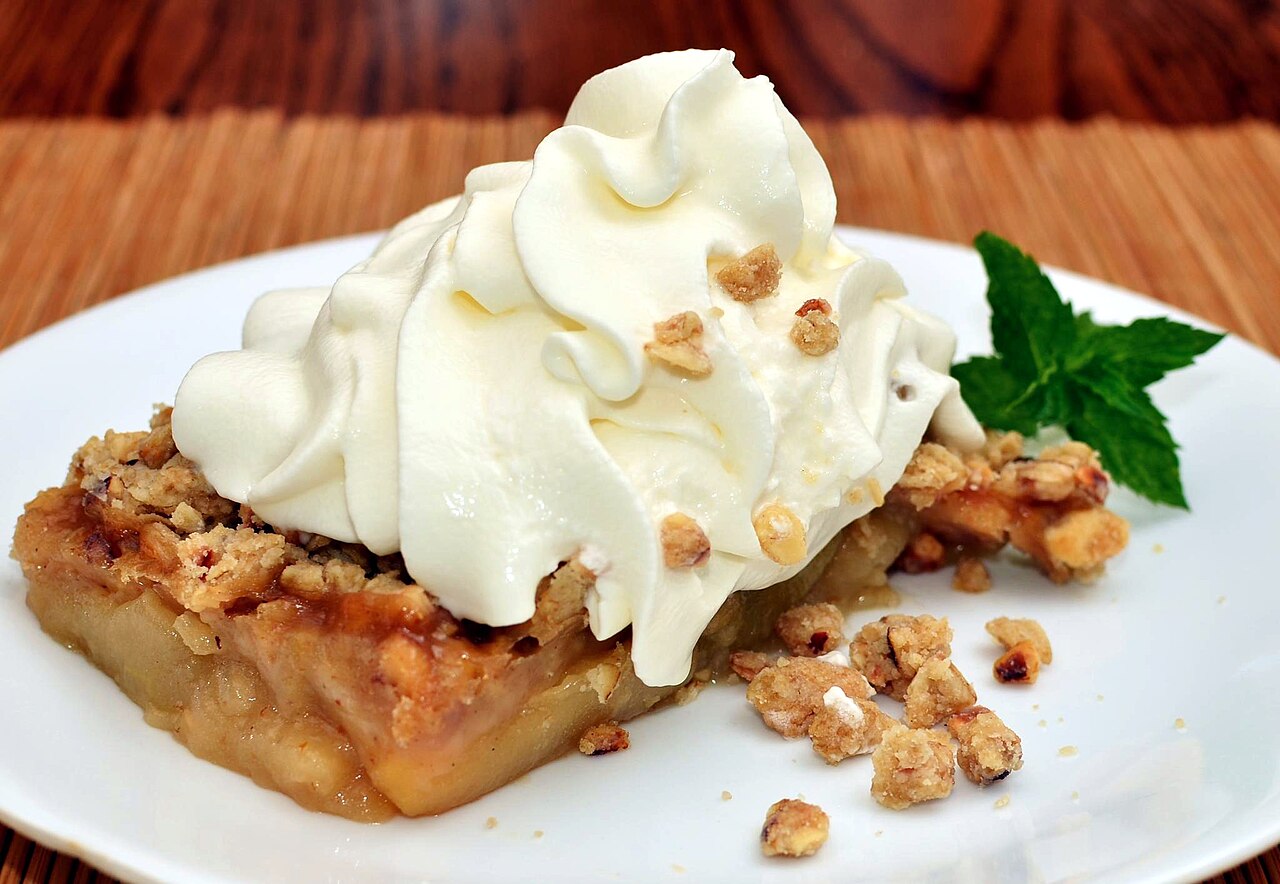 Slice of apple crisp topped with whipped cream and a sprig of mint on a white plate photo_0