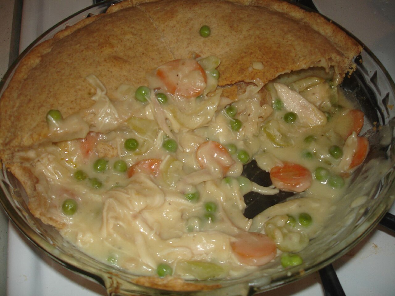 Homemade chicken pot pie in a glass pie dish with a golden crust and a creamy filling of chicken, carrots, and peas photo_0