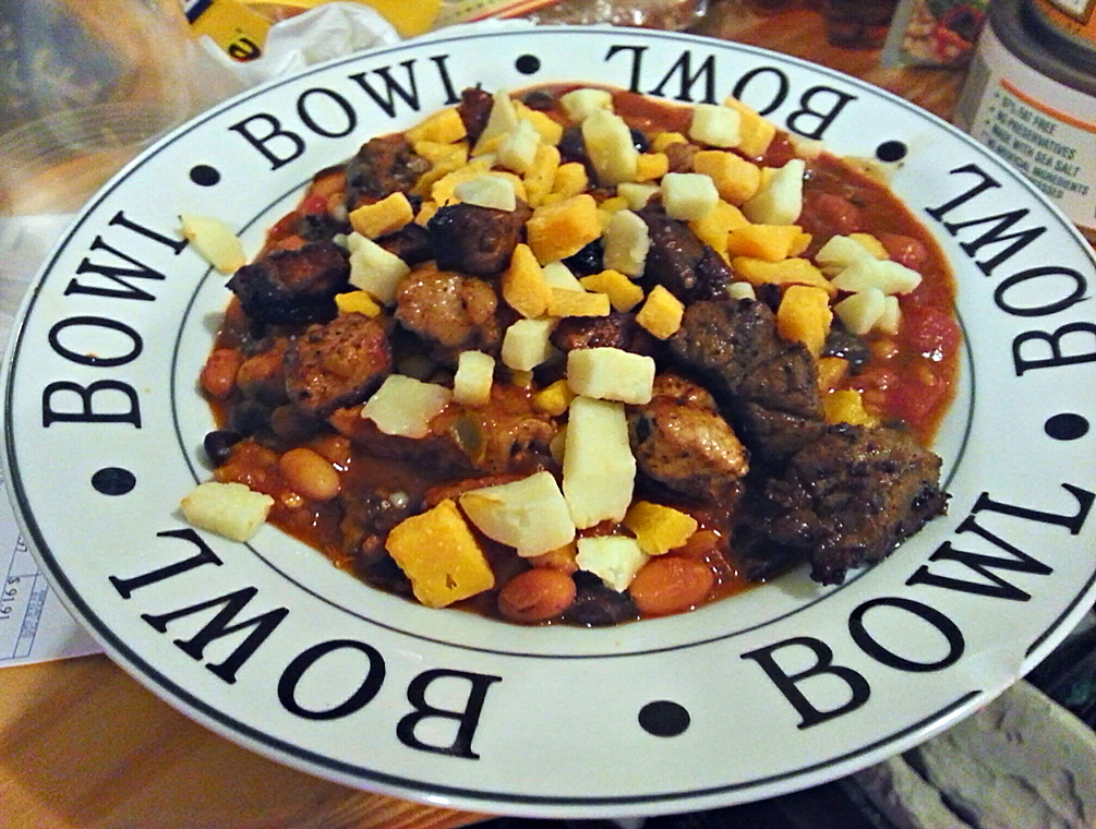 Bowl of chili with beans, a tomato base, and diced cheese on top, served in a white bowl-shaped plate photo_0 Bowl of chili with beans, a tomato base, and diced cheese on top, served in a white bowl-shaped plate photo_0